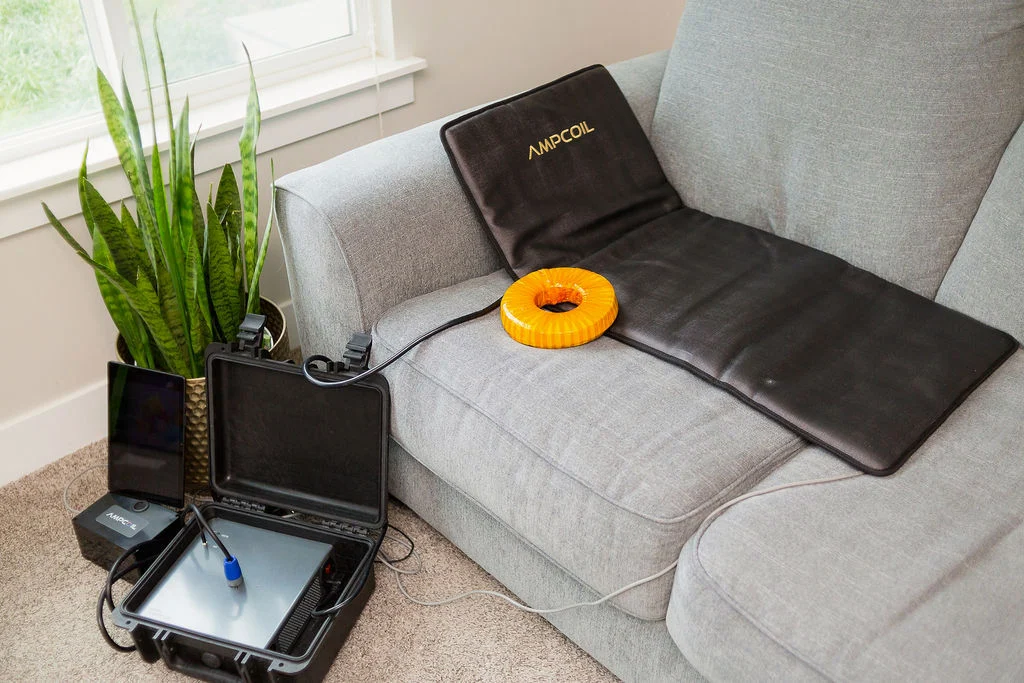 AmpCoil wellness system showing an electromagnetic coil, full-body PEMF mat, amplifier, and tablet arranged for a session.